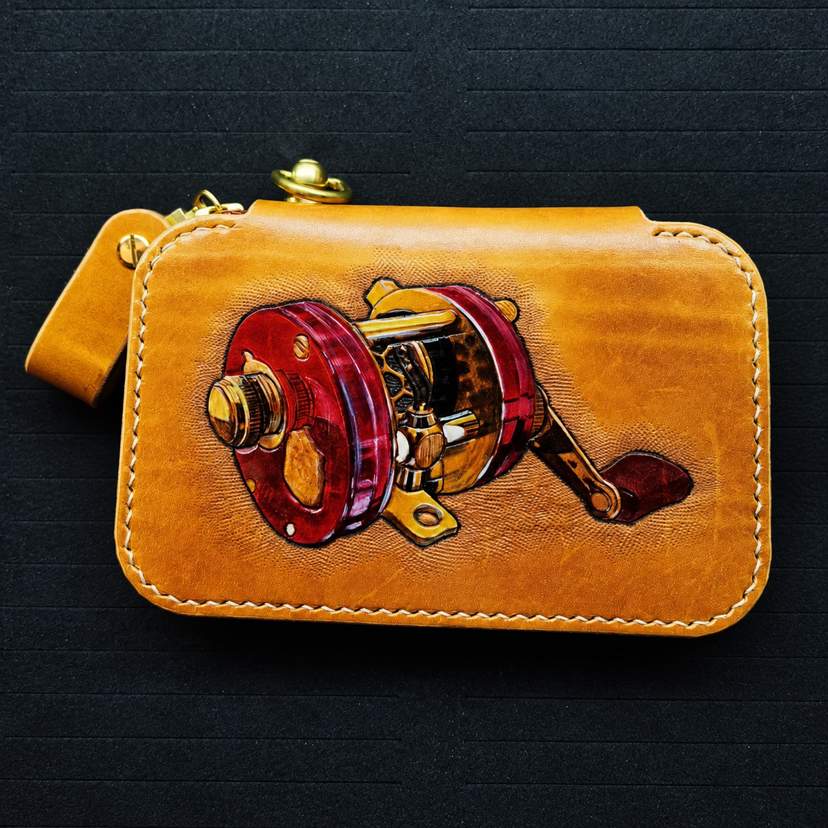 Red-and-gold fishing reel artwork on a leather wallet