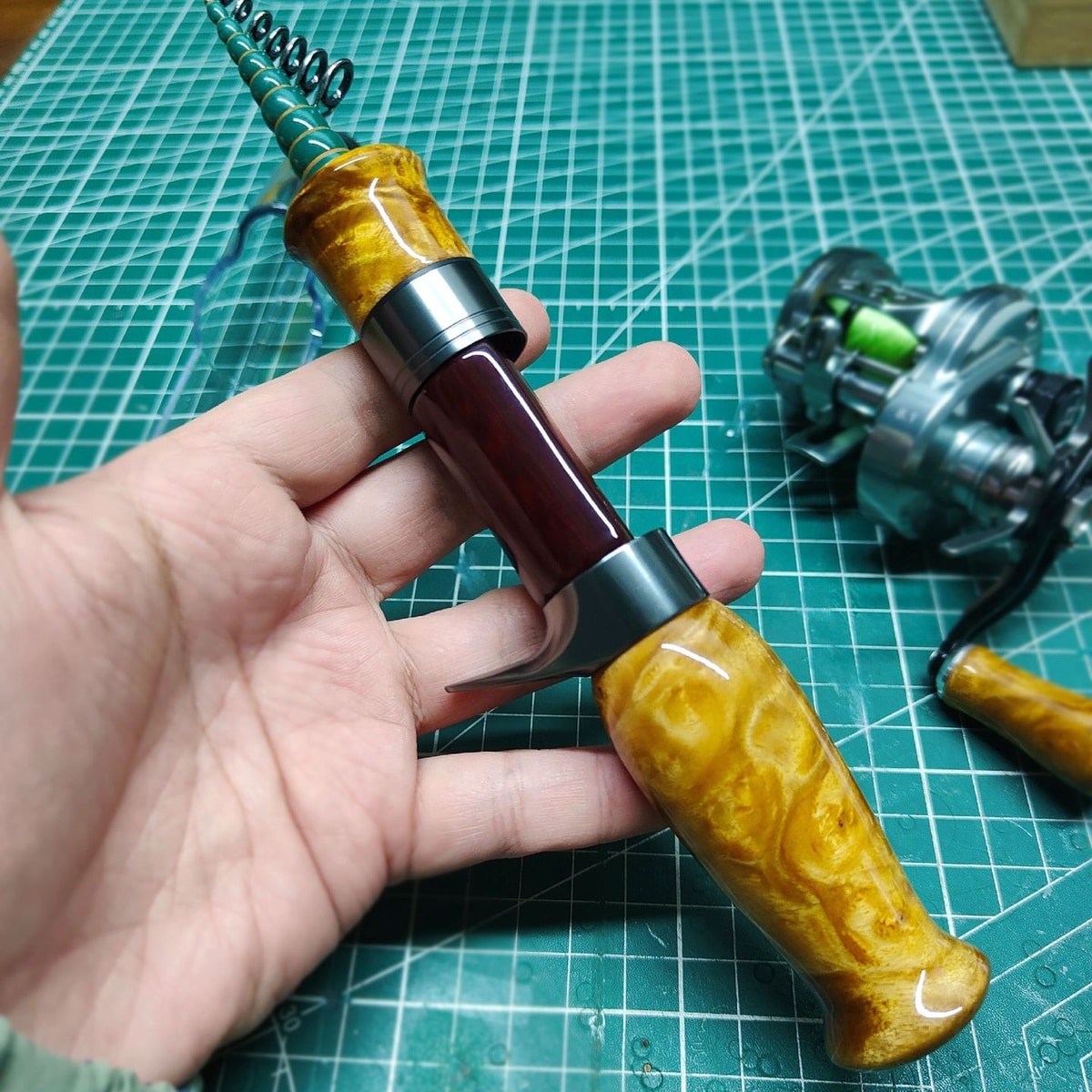 Close-up of the Atelier Contour sculpted golden-toned wood grip and red reel-seat insert held in a hand; reference build.