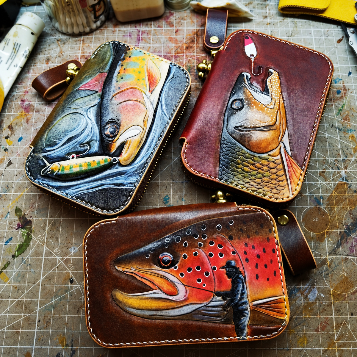Three hand-tooled leather lure wallet designs on a workbench; sold individually