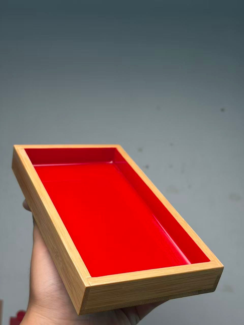 Original plain red urushi fish viewing box held at an angle, showing the lacquer interior and natural-grain frame