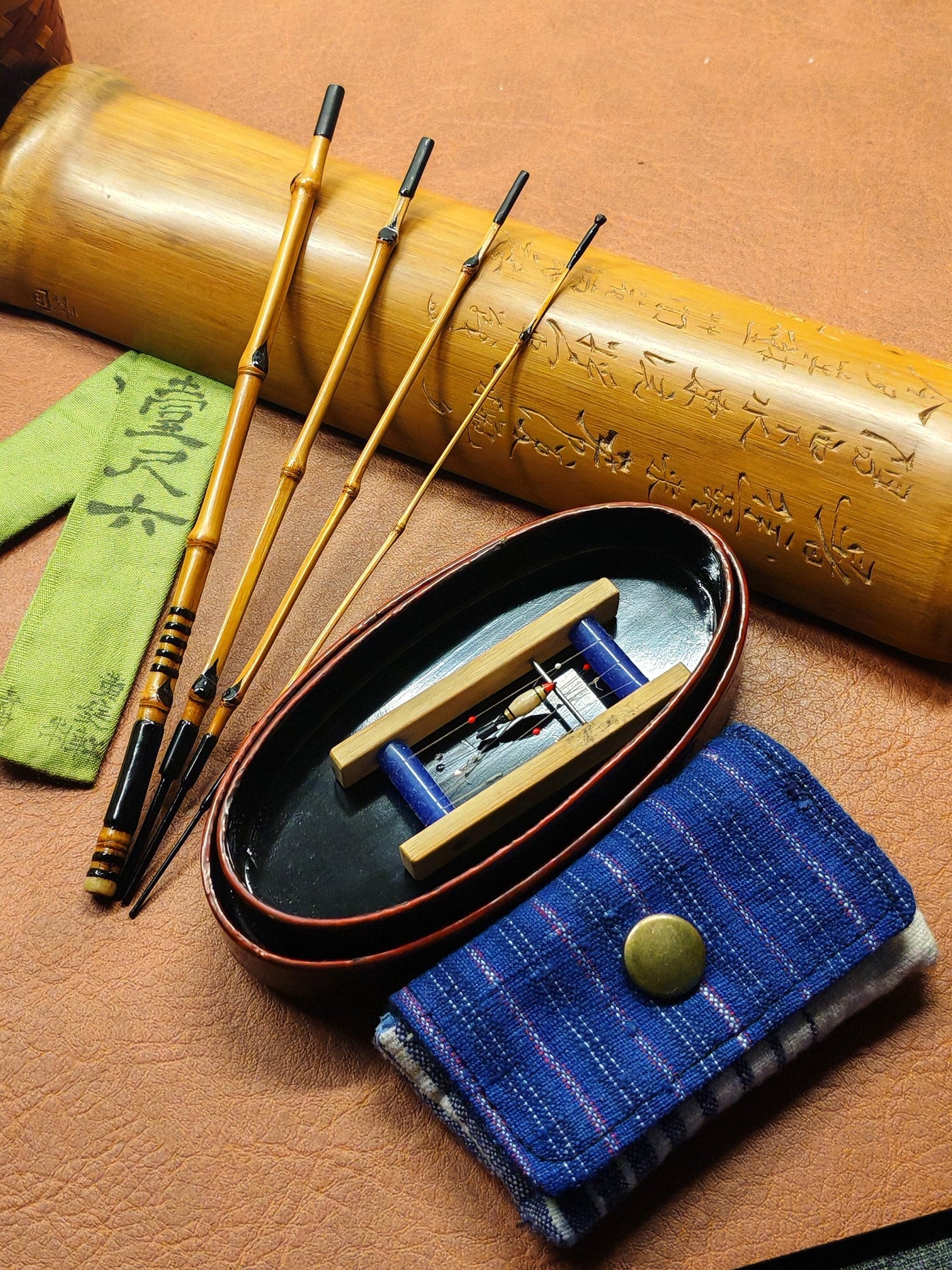 Handmade bamboo fishing rod sections beside a carved bamboo case and cloth sleeve